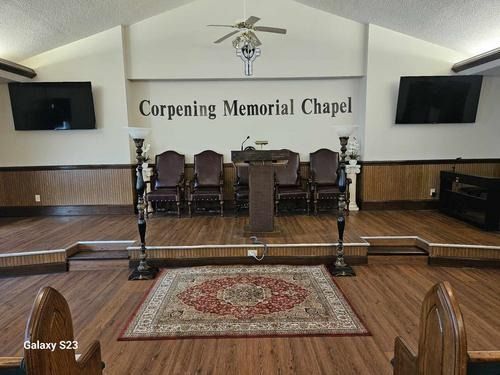Interior of Corpening Memorial Chapel with a wooden podium, chairs on a raised stage, and two mounted flat-screen TVs.