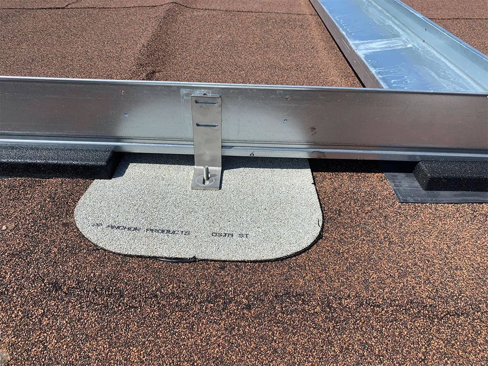 Metal bracket attached to a roof with a solar panel rail and a gray, rounded roof flashing.