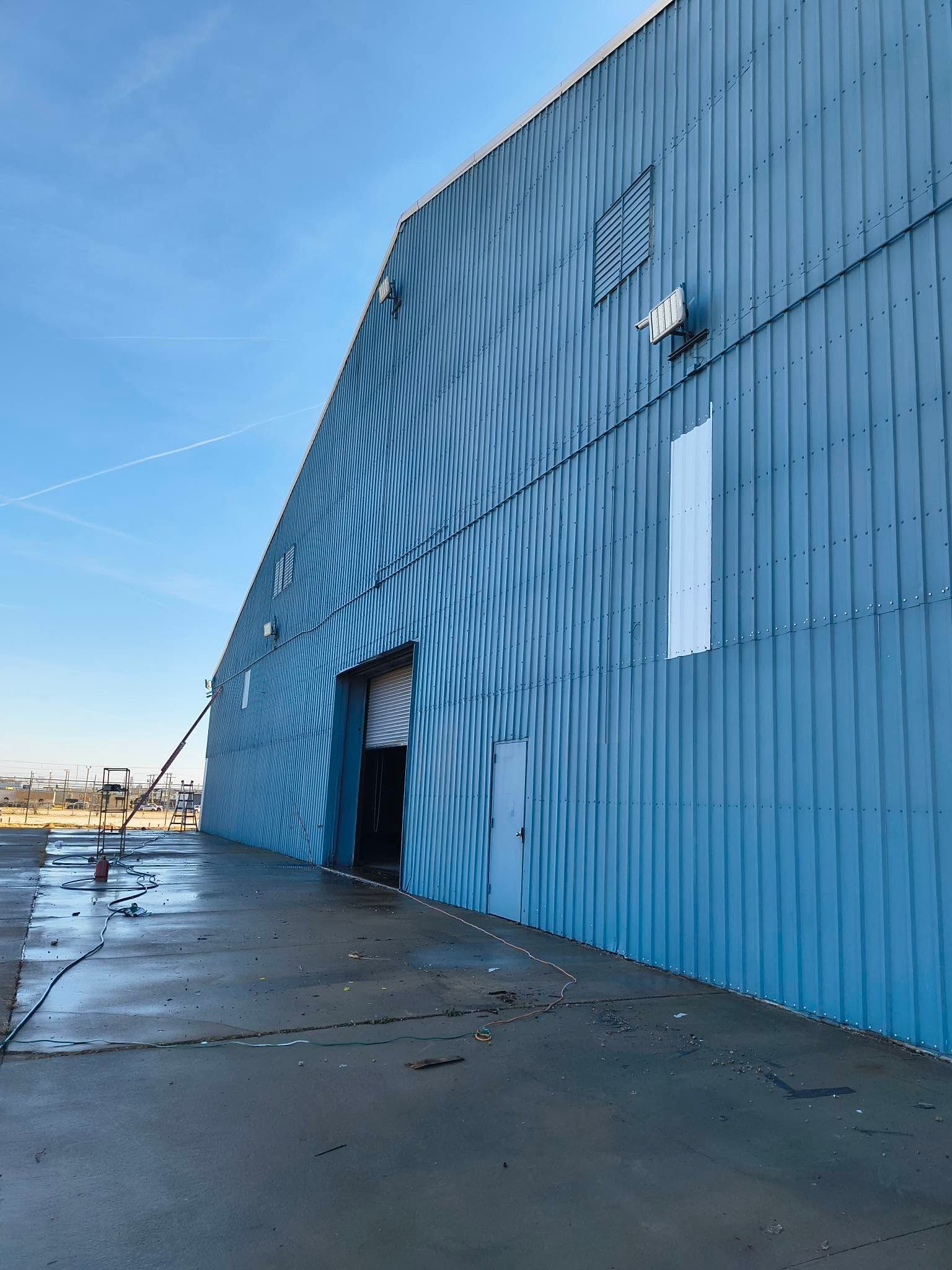 Blue corrugated metal building with wave mural, arched doorway, and wet sidewalk under a clear sky