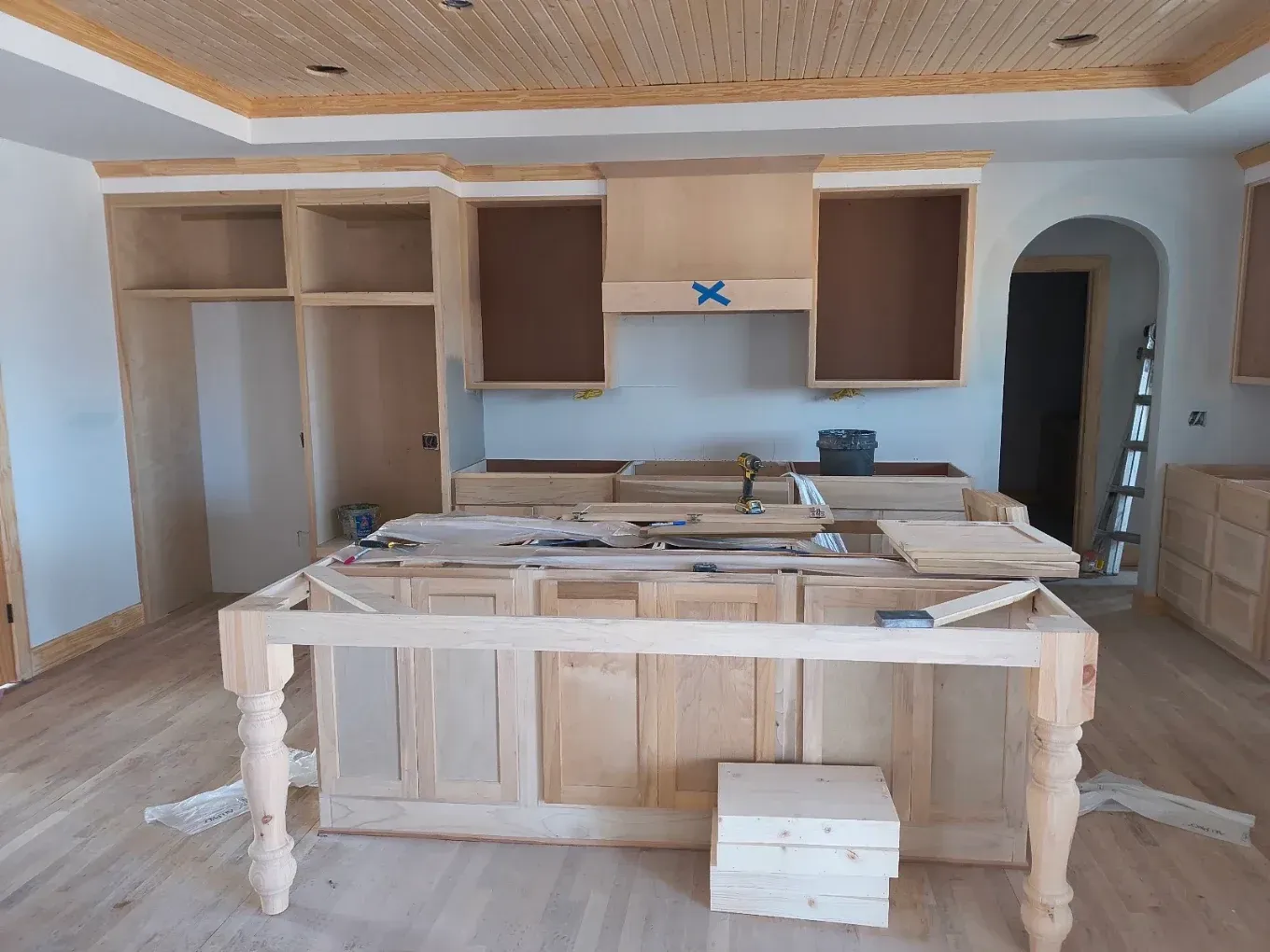 Unfinished kitchen with open cabinets, island, and construction materials on the floor
