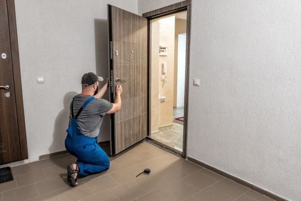 Man in blue coveralls installing a door lock in a doorway. Interior shot.