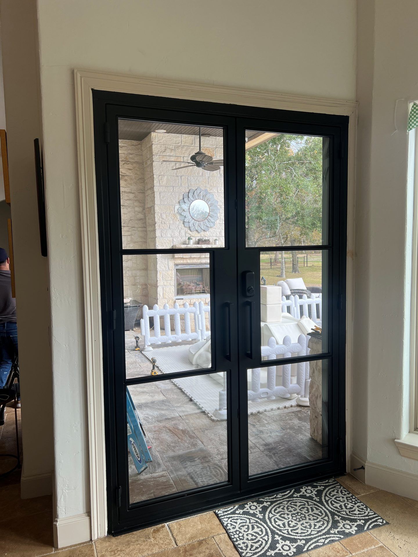 Black double glass doors opening to a stone patio with white outdoor furniture and a patterned doormat