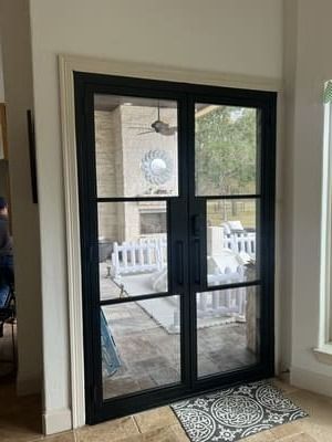 Black-framed double glass doors open to a white patio with chairs and a ceiling fan.