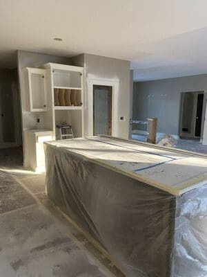 Kitchen under renovation with white cabinets, a wrapped island, and unfinished flooring