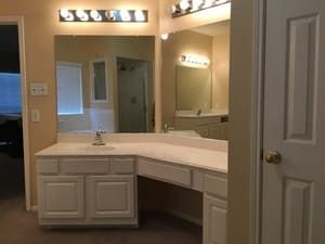 Bathroom vanity with large mirror, lights, and white cabinets under a beige wall.