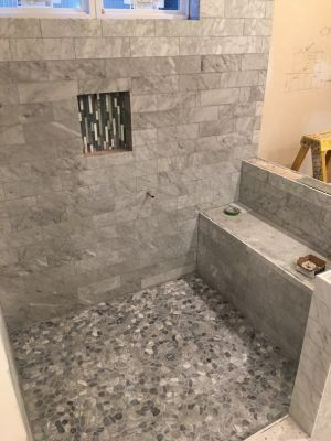 Partially tiled shower under construction with stone-look walls and a pebble floor, including a built-in bench.