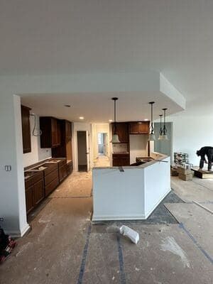 Partially renovated kitchen with white island, dark cabinets, pendant lights, and unfinished flooring