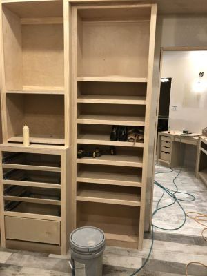 Built-in wooden closet under renovation with shelves, drawers, and a paint bucket on the floor