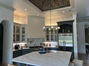 Modern white kitchen with marble island, glass cabinets, and ornate ceiling detail
