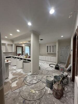 Renovation scene in a kitchen with white cabinets, tools, and construction debris on the floor
