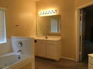 Bathroom with white vanity, lit mirror, bathtub, and beige walls