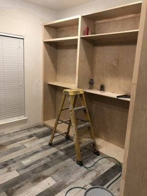 Built-in wooden shelves in a room, with a yellow step ladder and a window with blinds.