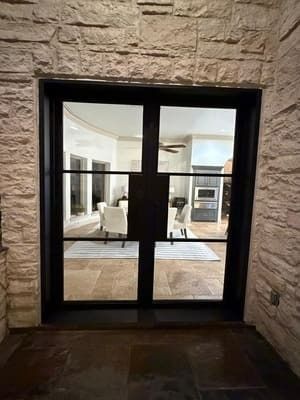 Stone entryway with black-framed glass double doors opening into a bright interior room
