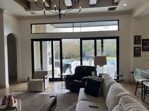 Bright living room with large glass doors, white sofa, and dark armchair facing a pool outside
