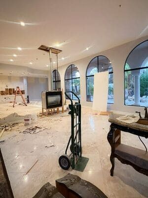 Renovated living room with arched windows, fireplace, and moving cart amid construction debris