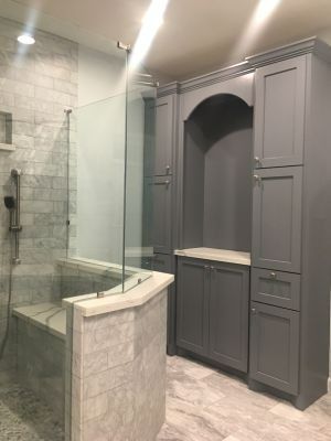 Modern bathroom with glass shower, white tile, and gray built-in cabinets