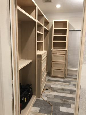 Narrow walk-in closet under construction with unfinished wood shelves, drawers, and a hanging rod.