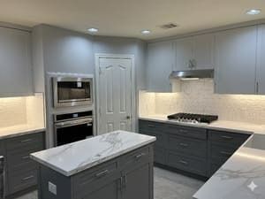 Modern gray kitchen with island, built-in oven, gas range, and white marble countertops.