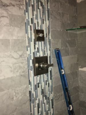 Bathroom wall with tiled shower fixture and a blue level leaning beside it