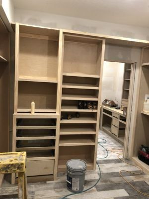 Unfinished built-in closet shelves in a room under construction, with tools and a paint bucket on the floor.
