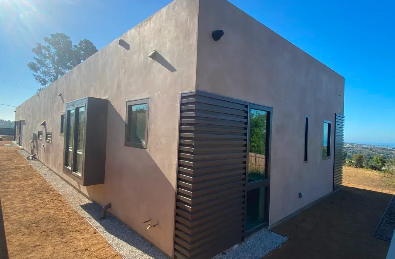 Tan stucco house with brown shutters, windows, and blue sky background.