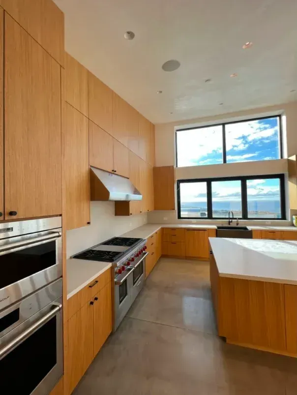 Modern kitchen with light wood cabinetry, stainless steel appliances, and large windows with ocean views.