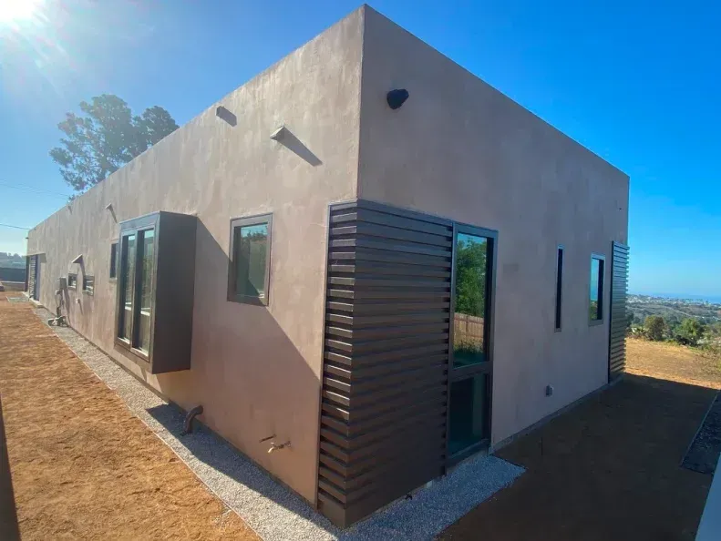 Modern, beige house with brown shutters and windows on a sunny day.