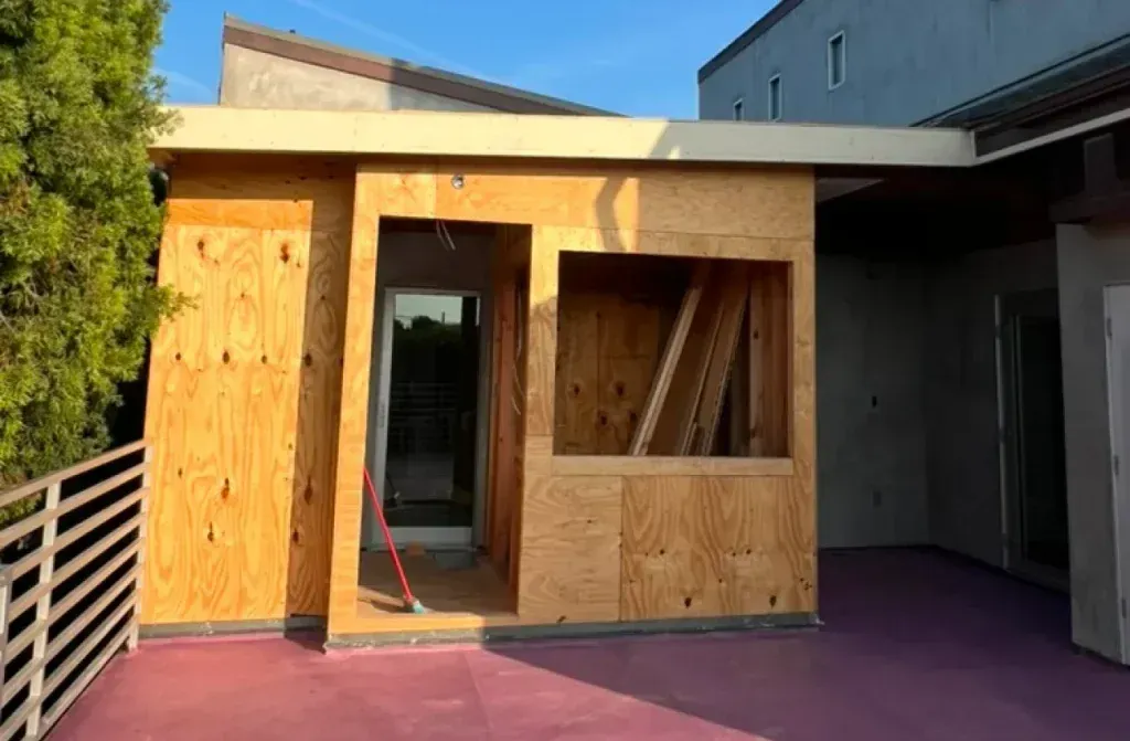 Wooden structure under construction on a red patio with an open doorway and window.