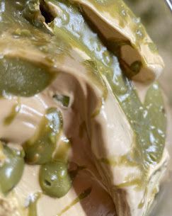Primo piano di un dessert cremoso, liscio e di colore marrone chiaro, con striature di sciroppo verde brillante e piccole sfere verdi.