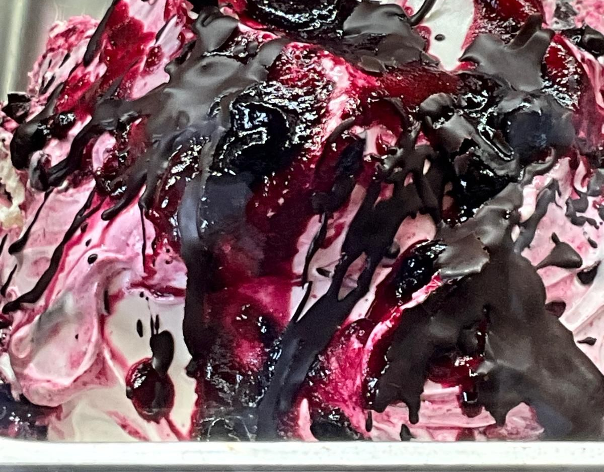Un primo piano di gelato con una spirale di marmellata di frutti di bosco viola acceso e guarnito con spesse strisce di cioccolato fondente.