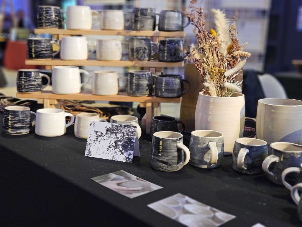 Display of handmade ceramic mugs and cups on shelves and a table at a market stall