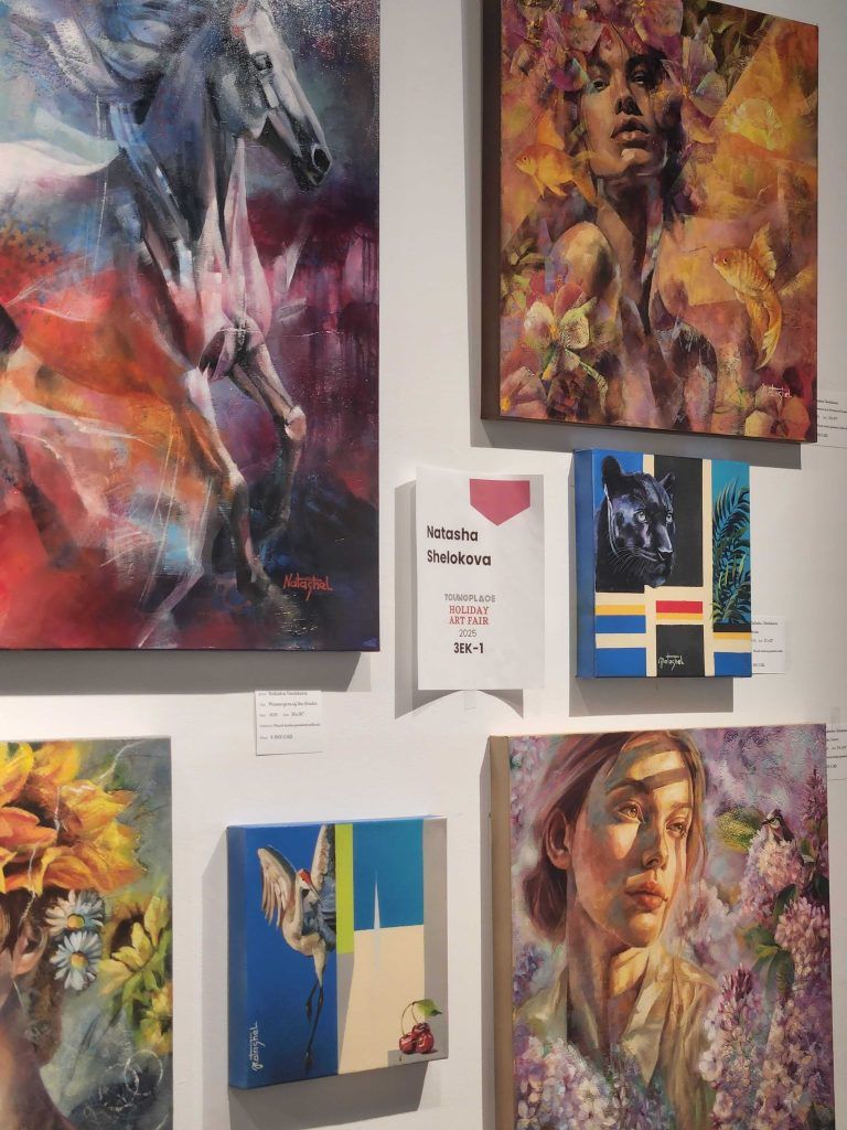 Gallery wall of colorful abstract and portrait paintings with a small central sign