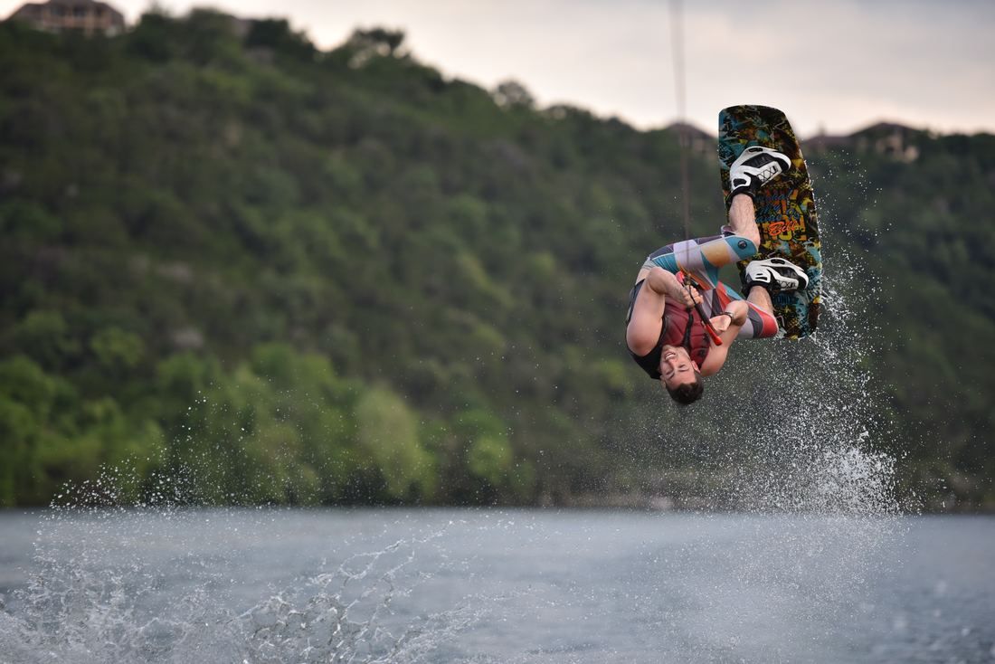 A man is doing a trick on a wakeboard over a lake.
