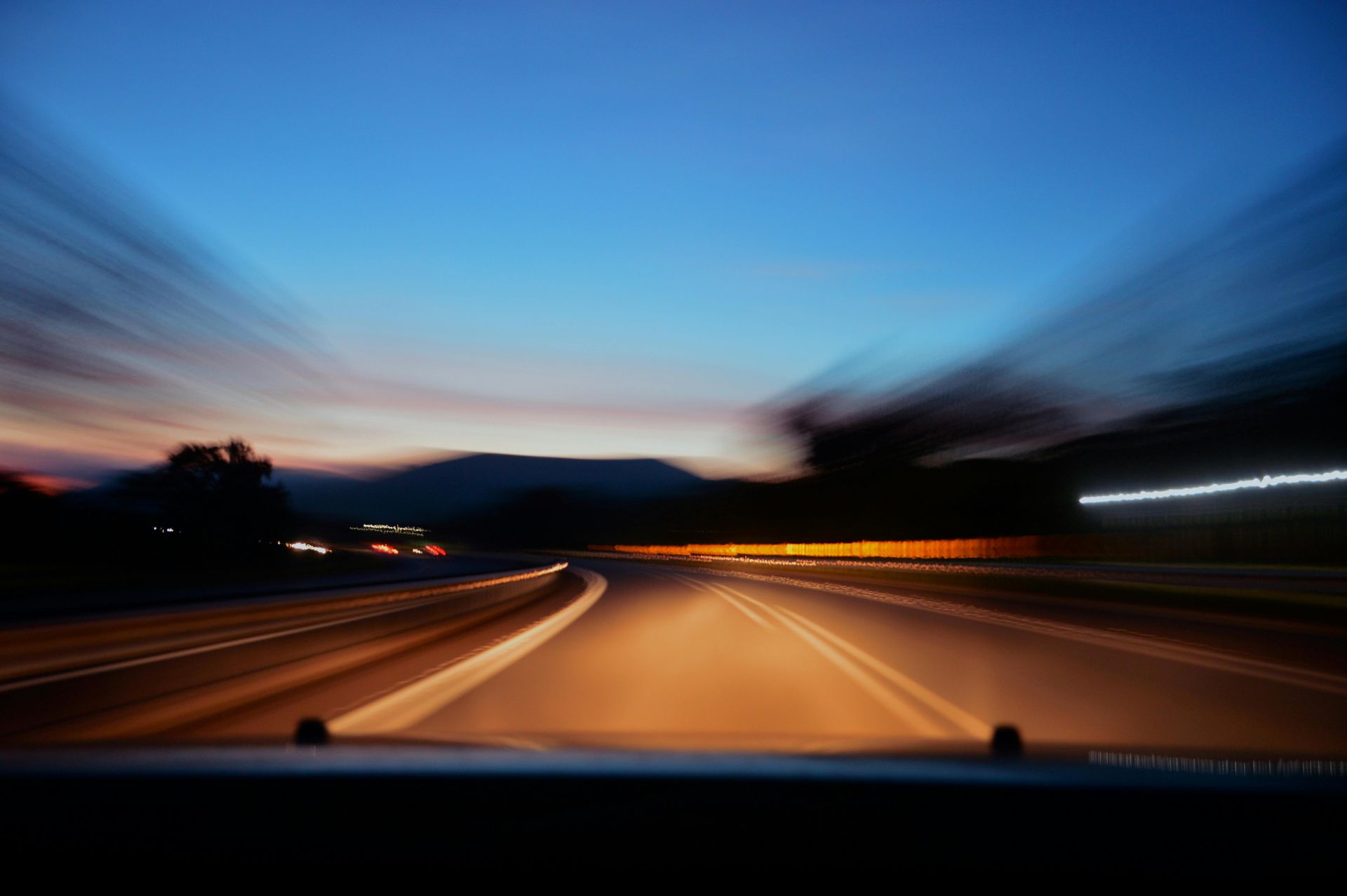 Car driving at dusk on a highway with blurred lights and a colorful sky.