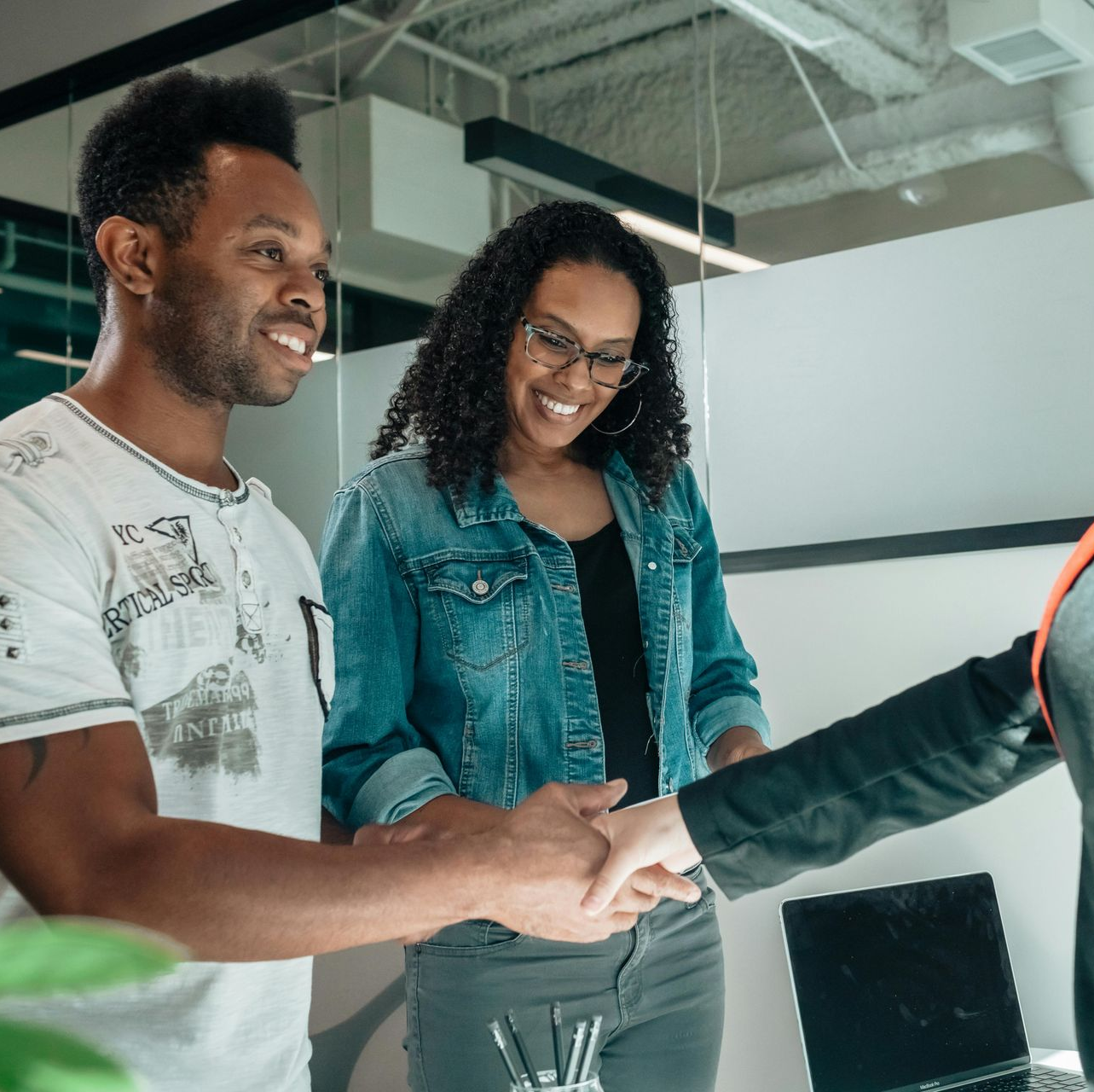 Two people shaking hands in an office setting. Smiling man and woman in denim look on.