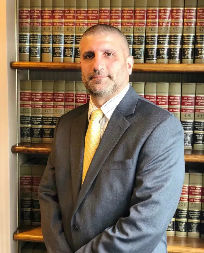 Man in gray suit with yellow tie stands in front of bookshelves.