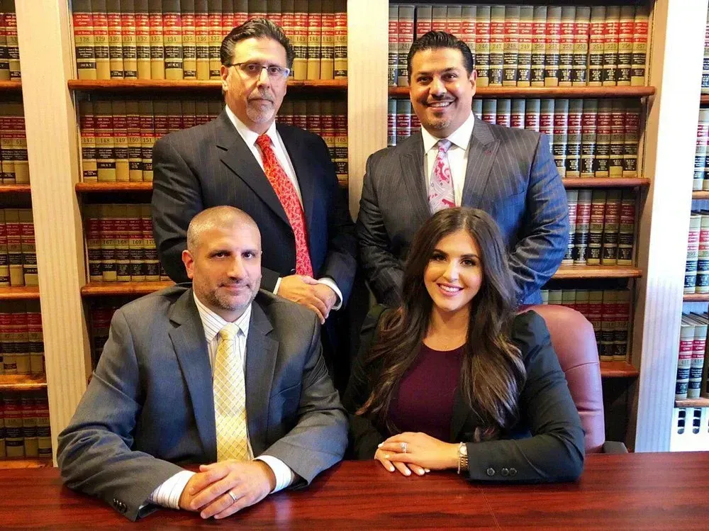 Four attorneys in suits, posing for a group photo in a library setting, with bookshelves in the background.
