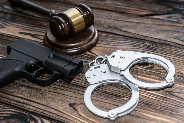 Gavel, handgun, and handcuffs on a wooden surface, suggesting legal and law enforcement themes.