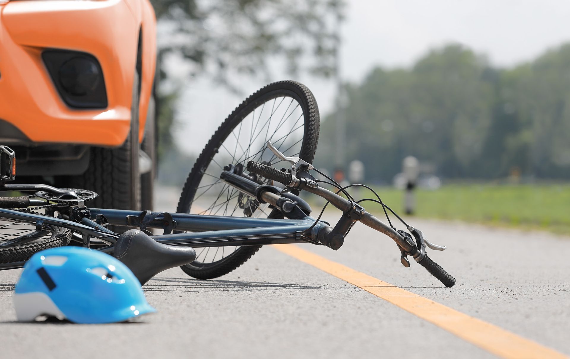 Orange car and bicycle on a road after a collision; a blue helmet lies nearby.