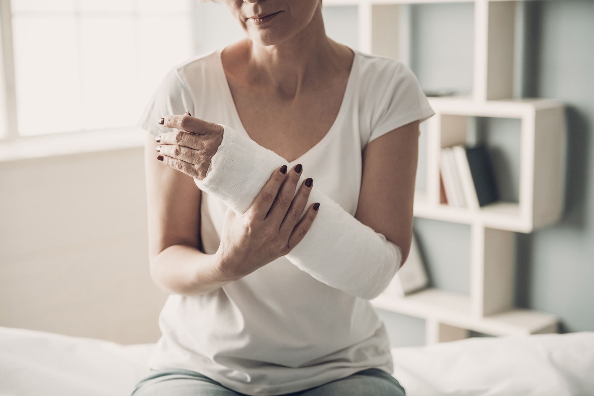 Woman with arm in white cast, sitting indoors, showing pain.