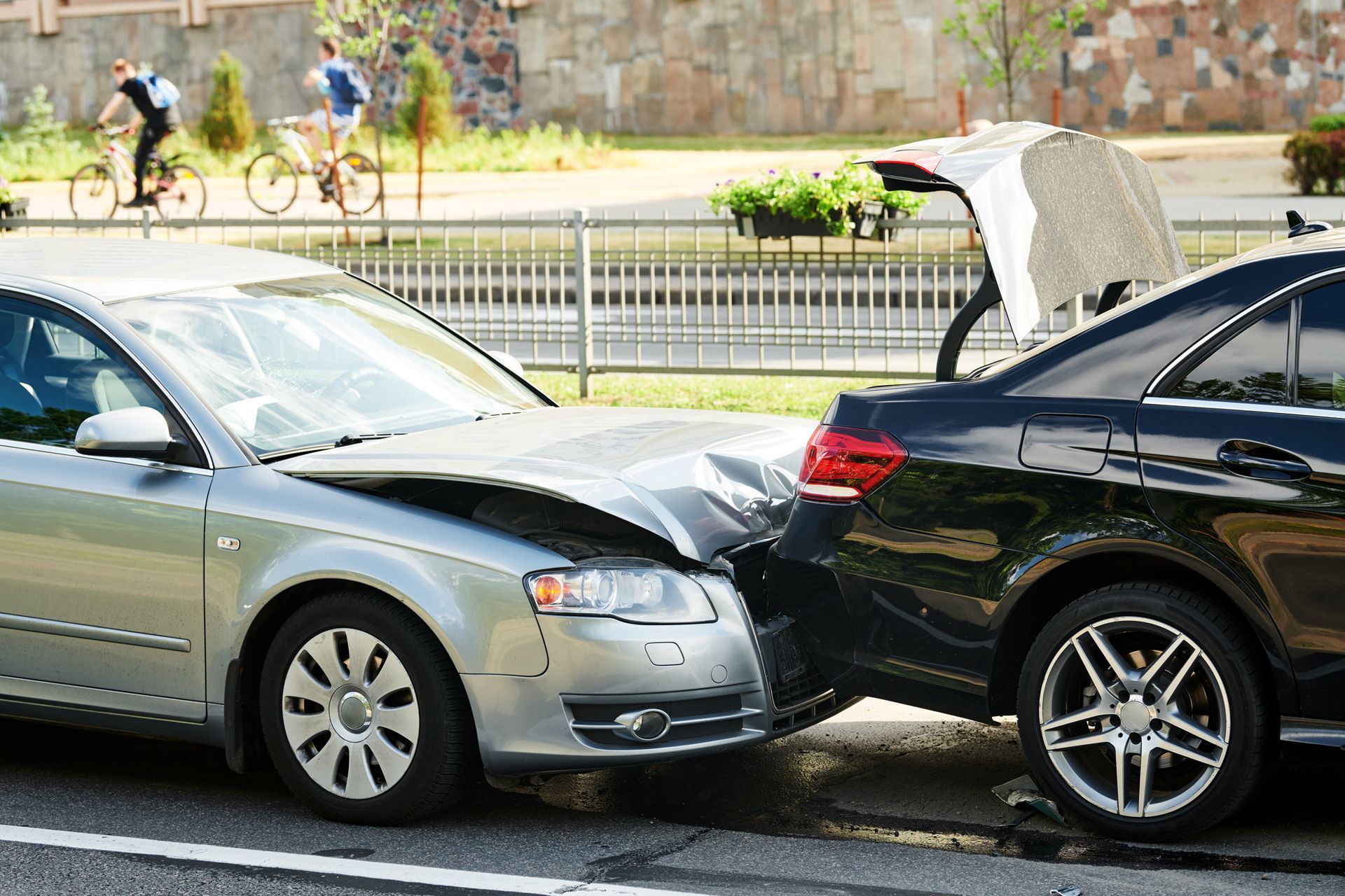 Two cars, silver and black, damaged in a collision on a city street.