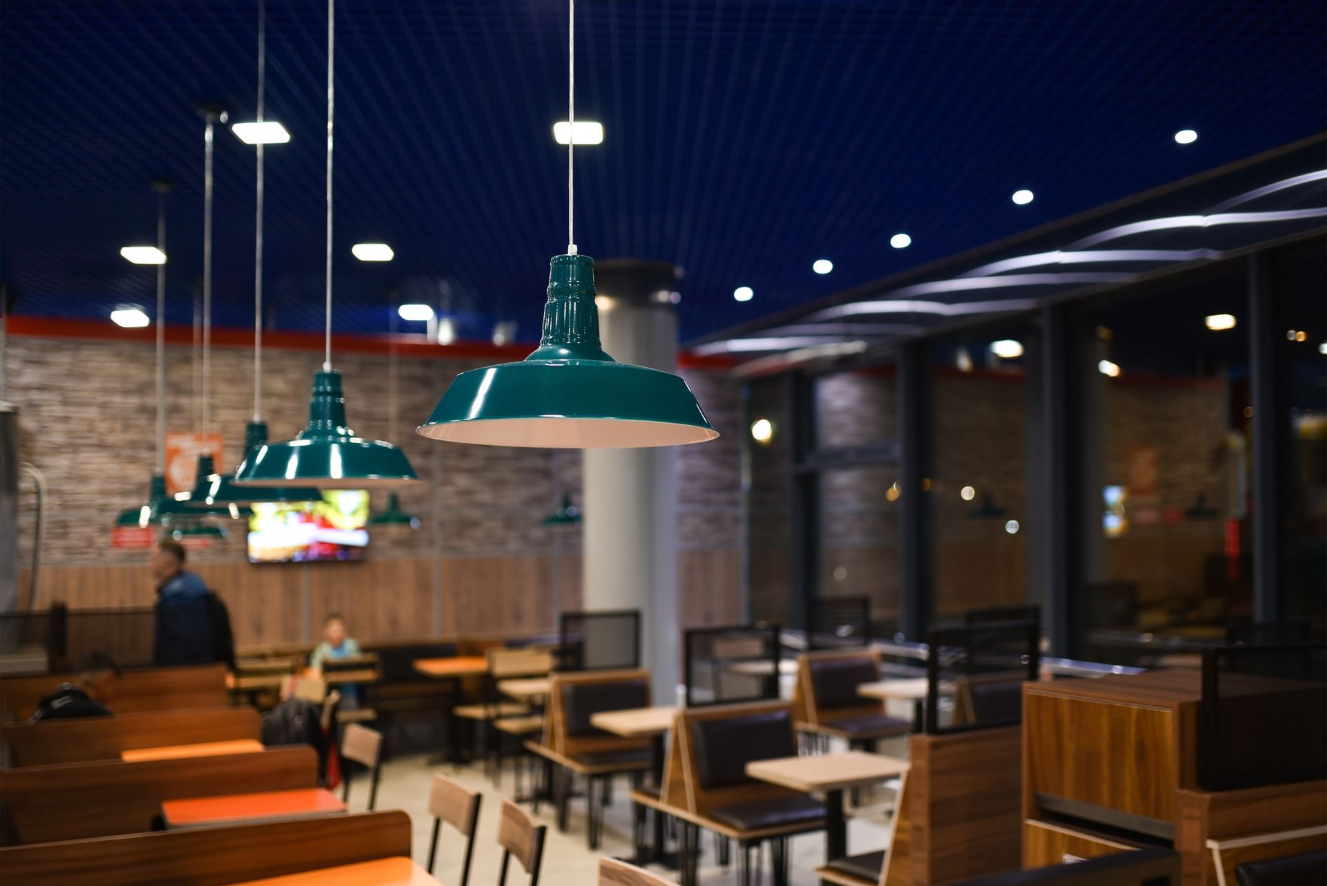 Restaurant interior with teal pendant lights, wooden tables and chairs.