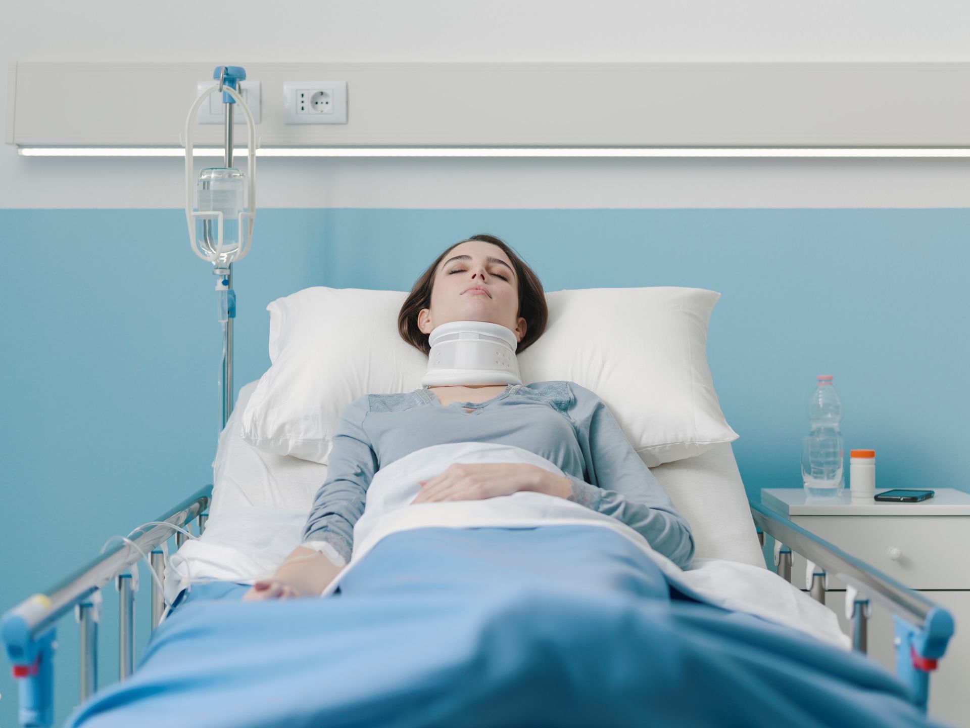 Woman in hospital bed wearing neck brace, receiving IV fluids.