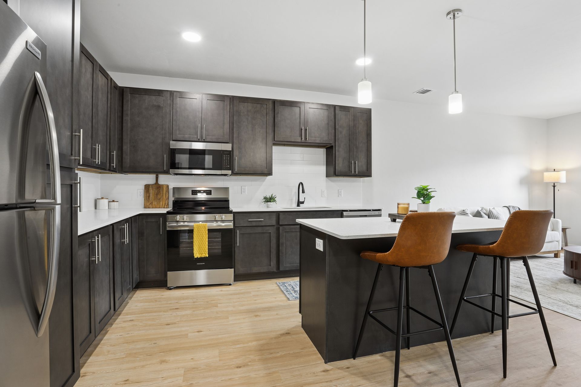 Modern kitchen with dark cabinets, stainless appliances, island seating, and light wood flooring