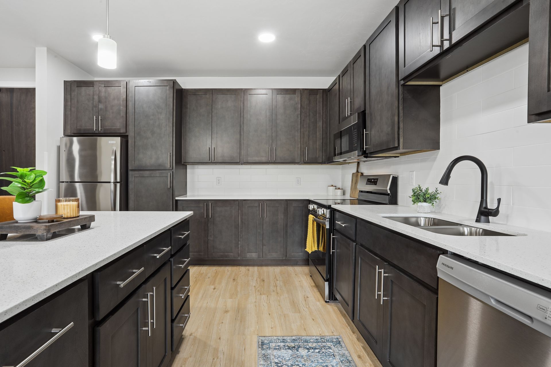 Modern kitchen with dark cabinets, stainless steel appliances, white countertops, and a central island