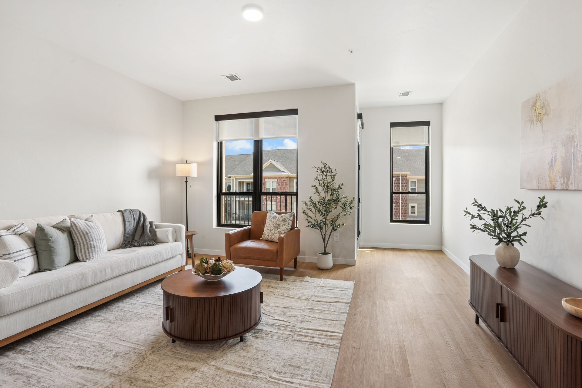 Bright modern living room with white sofa, wooden coffee table, large windows, and light wood floors