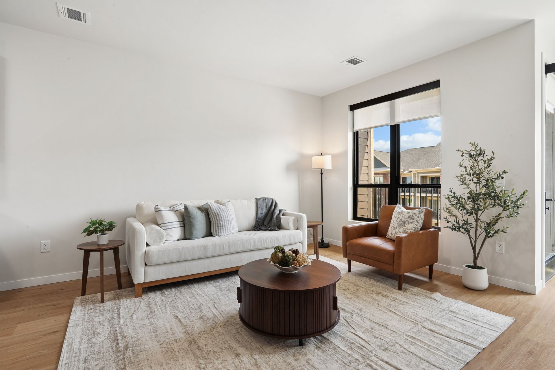 Bright modern living room with white sofa, brown chairs, round coffee table, and large window view
