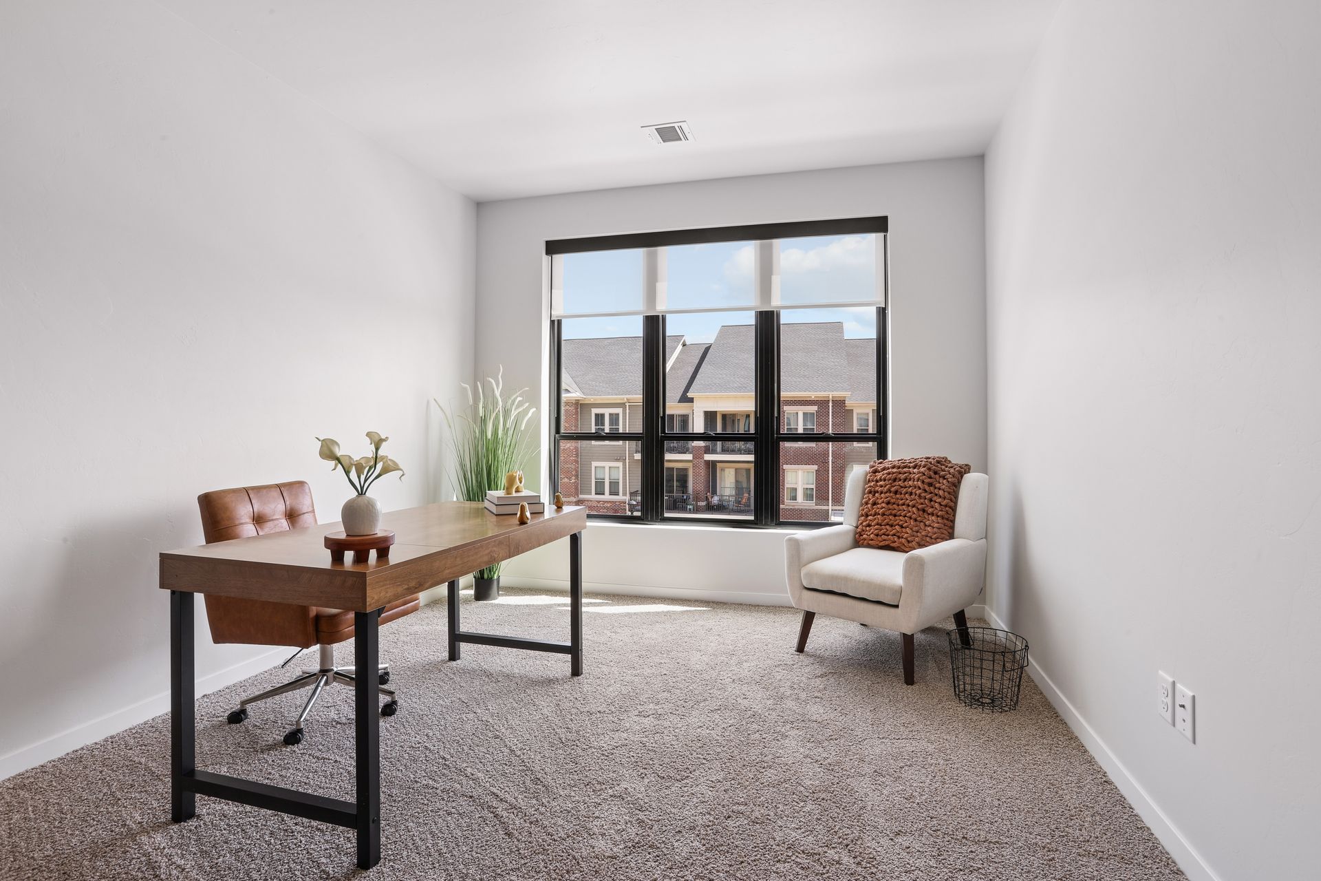 Bright home office with desk, chair, and large window overlooking apartment buildings