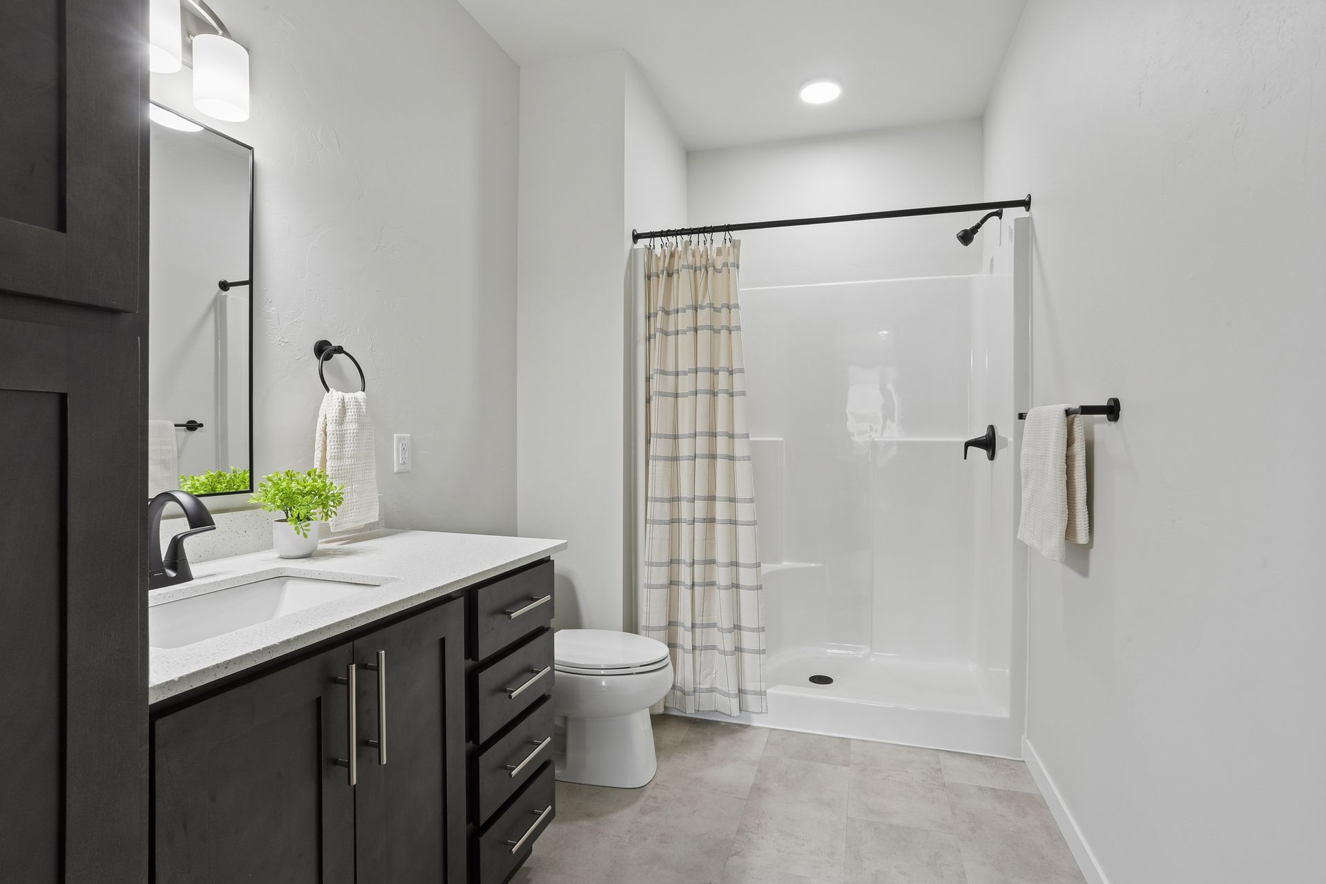 Modern bathroom with dark vanity, white tub shower, and beige tile flooring