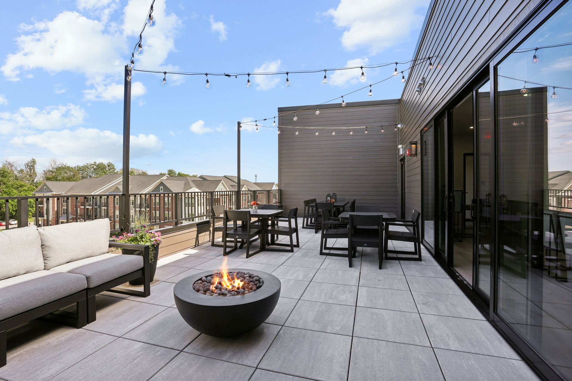 Modern rooftop patio with outdoor seating, fire pit, string lights, and city views